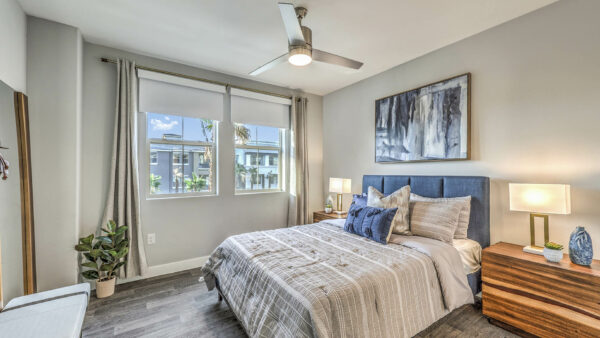 Bedroom with plush bed, wood bedside chests with lamps, ceiling fan, and large window.