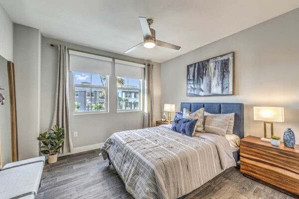 Bedroom with plush bed, wood bedside chests with lamps, ceiling fan, and large window.