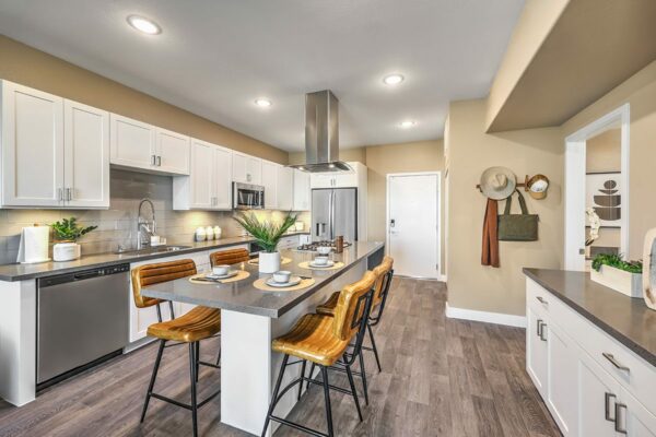 Apartment kitchen with wood style floor, white cabinets, stainless steel appliances, and breakfast bar with stools.