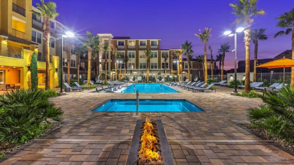 Pool area with fireplace, spa, stone paver patio, lounge chairs, and tall palm trees.