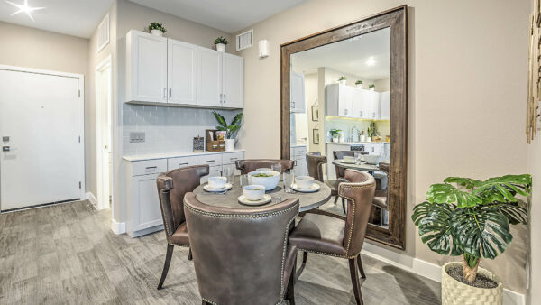 Dining room with wood floor, dining table with leather chairs, gray cabinets, and large framed mirror.