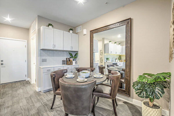 Dining room with wood floor, dining table with leather chairs, gray cabinets, and large framed mirror.