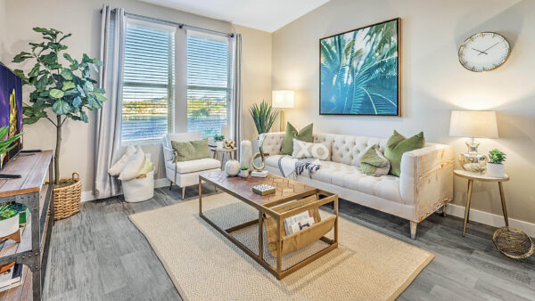 Living room with wood floor, plush seating, tables with decor, framed artwork, and large window.