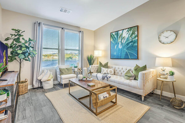 Living room with wood floor, plush seating, tables with decor, framed artwork, and large window.