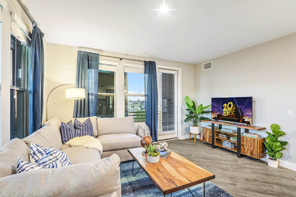 Living room with wood floor, plush couch, wood table with decor, and door to balcony.