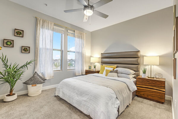 Bedroom with carpet, plush bed with headboard, bedside drawers with lamps, and large windows.