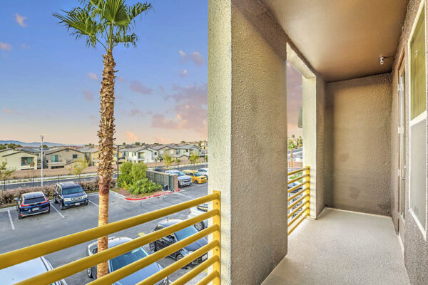 Balcony with metal railing overlooking parking area with tall palms.
