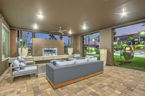 Indoor/outdoor lounge with stone paver patio, plush seating, ceiling fan, and fireplace.