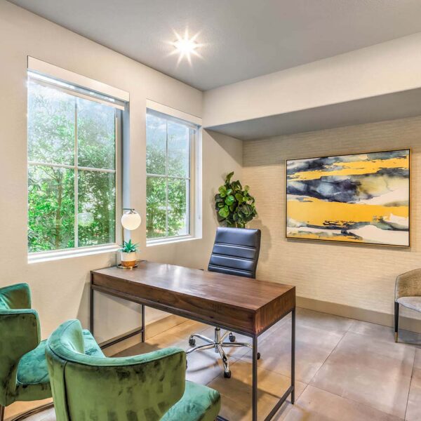 Office with desk, plush green chairs, large windows, and artwork.