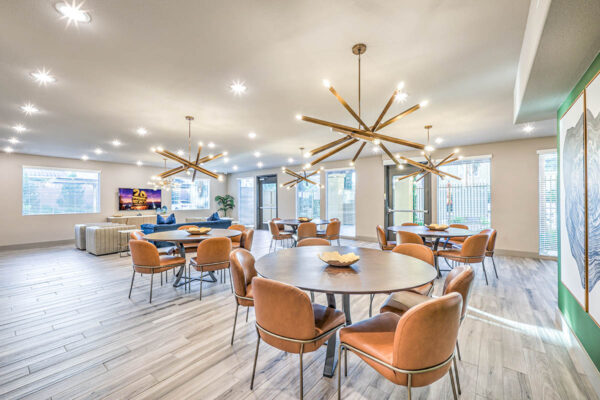 Lounge with dining tables, bronze chandeliers, large artwork, and TV.