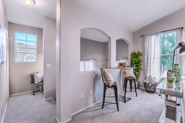 Living area with stairway, dining table with stools, built in computer desk, and large windows.
