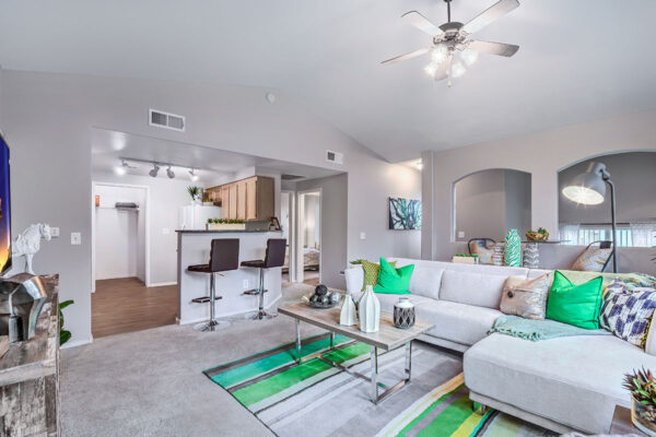 Living room with carpet, plush seating, ceiling fan, shelves with decor, and breakfast bar.