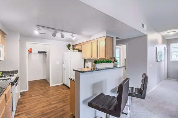 Kitchen with wood floor and cabinets, stone counters, white appliances, and breakfast bar with stools.