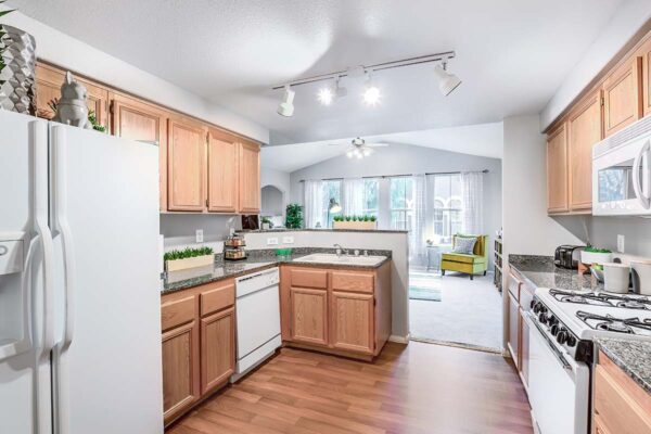 Kitchen with wood floor and cabinets, stone counters, white appliances, and breakfast bar.