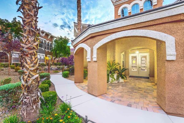 Chateau Calais office entrance with elegant architecture, lush landscaping, and tall palm trees.