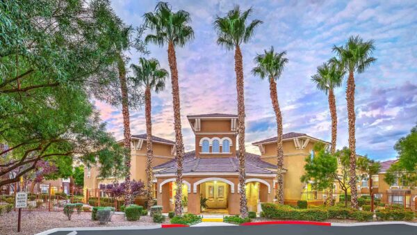 Chateau Calais office entrance with elegant architecture, lush landscaping, and tall palm trees.