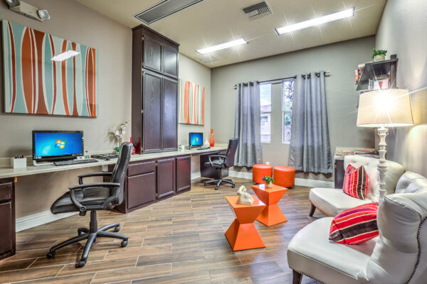 Business center with computer desks, shelves with books and decor, plush seats, and large window.