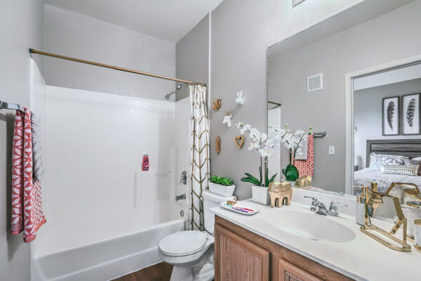 Bathroom with wood cabinets, white counters, large mirror, and tiled shower tub.