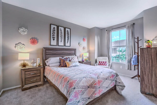 Bedroom with plush bed, wood bedside chests with lamps, dresser with decor, and large window.