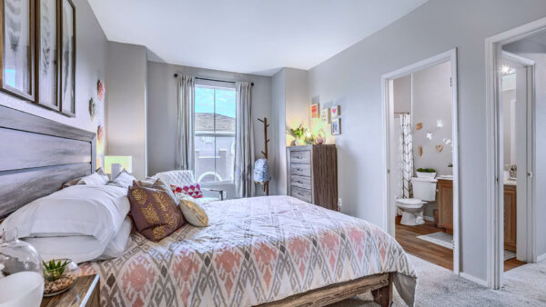 Bedroom with plush bed, wood bedside chests with lamps, dresser with decor, and large window.