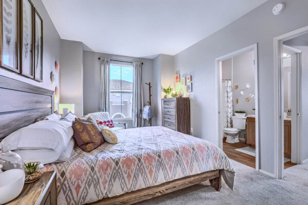 Bedroom with plush bed, wood bedside chests with lamps, dresser with decor, and large window.