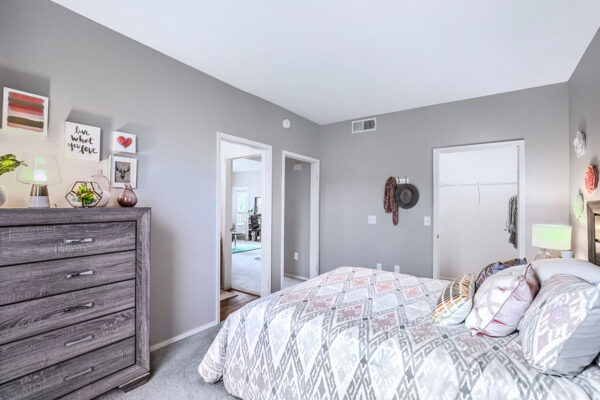 Bedroom with plush bed, wood bedside chests with lamps, dresser with decor, and large window.