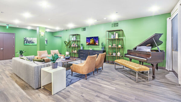Lounge with wood floor, comfortable seating, piano, shelves with decor, and TV.