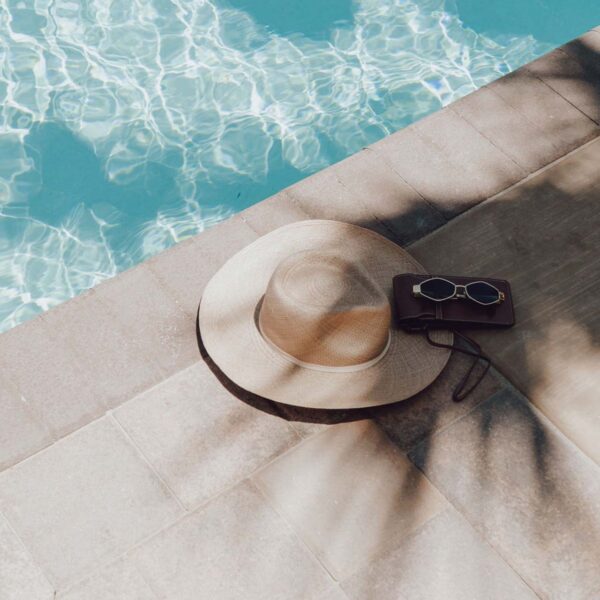 Hat, purse, and sunglasses next to shimmering pool.