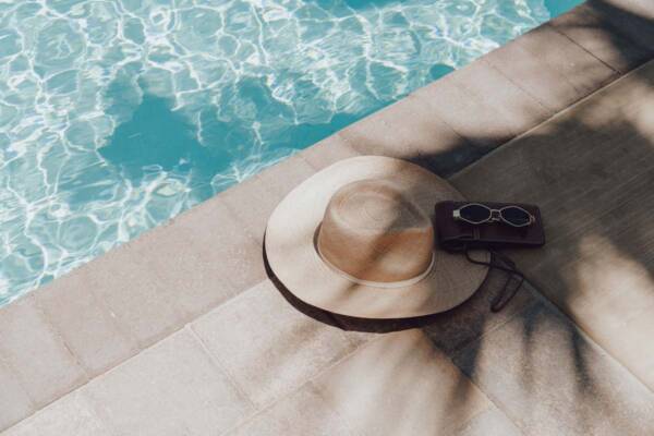 Hat, purse, and sunglasses next to shimmering pool.