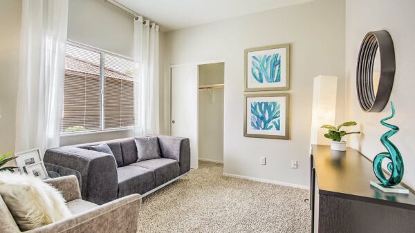 Living room with carpet, plush seating, console with decor, framed artwork, and large window.