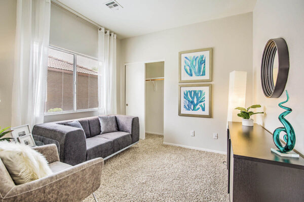 Living room with carpet, plush seating, console with decor, framed artwork, and large window.