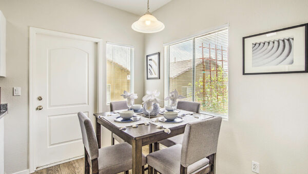Dining room with wood floor, tall table with stools, framed artwork, and large windows.