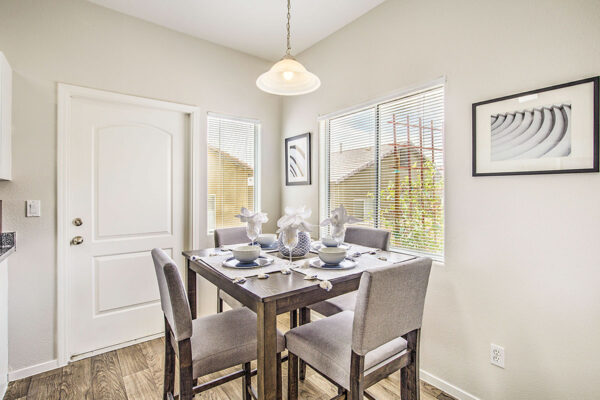 Dining room with wood floor, tall table with stools, framed artwork, and large windows.