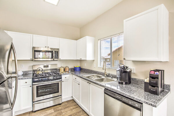 Kitchen with wood floor, white cabinets, stone counters, and stainless steel appliances.