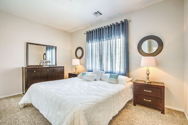 Bedroom with plush bed, bedside dressers with lamps, dresser with mirror, and large window.