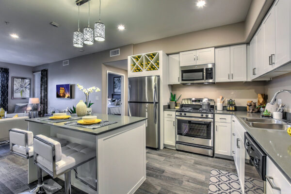 Kitchen with wood floor, white cabinets, grey counters, and stainless steel appliances.