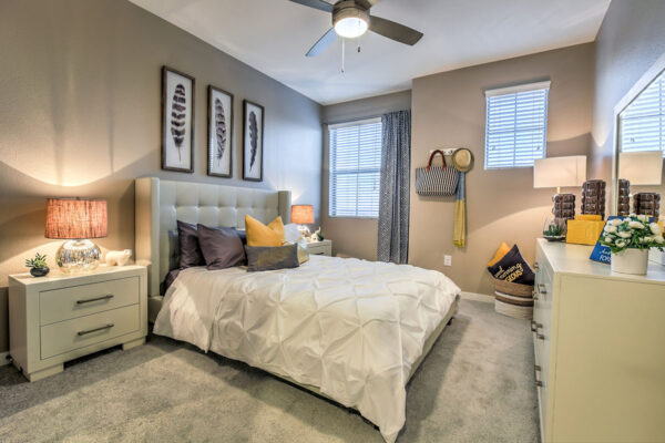Bedroom with carpet, plush bed with headboard, bedside drawers with lamps, and dresser with mirror.