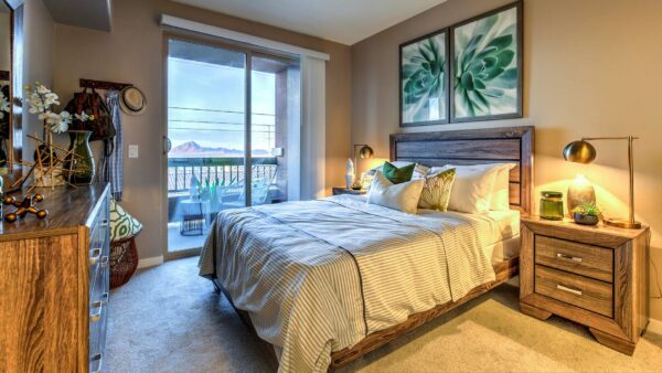 Bedroom with carpet, wood bed with headboard, bedside drawers with lamps, and balcony door.