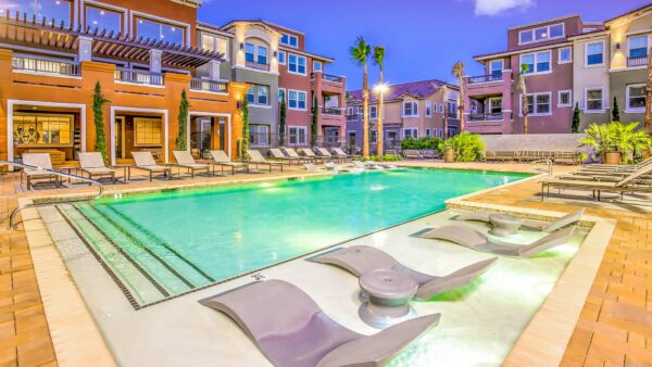 Pool area with stone paver patio, lounge chairs, rooftop patio, and tall palm trees.
