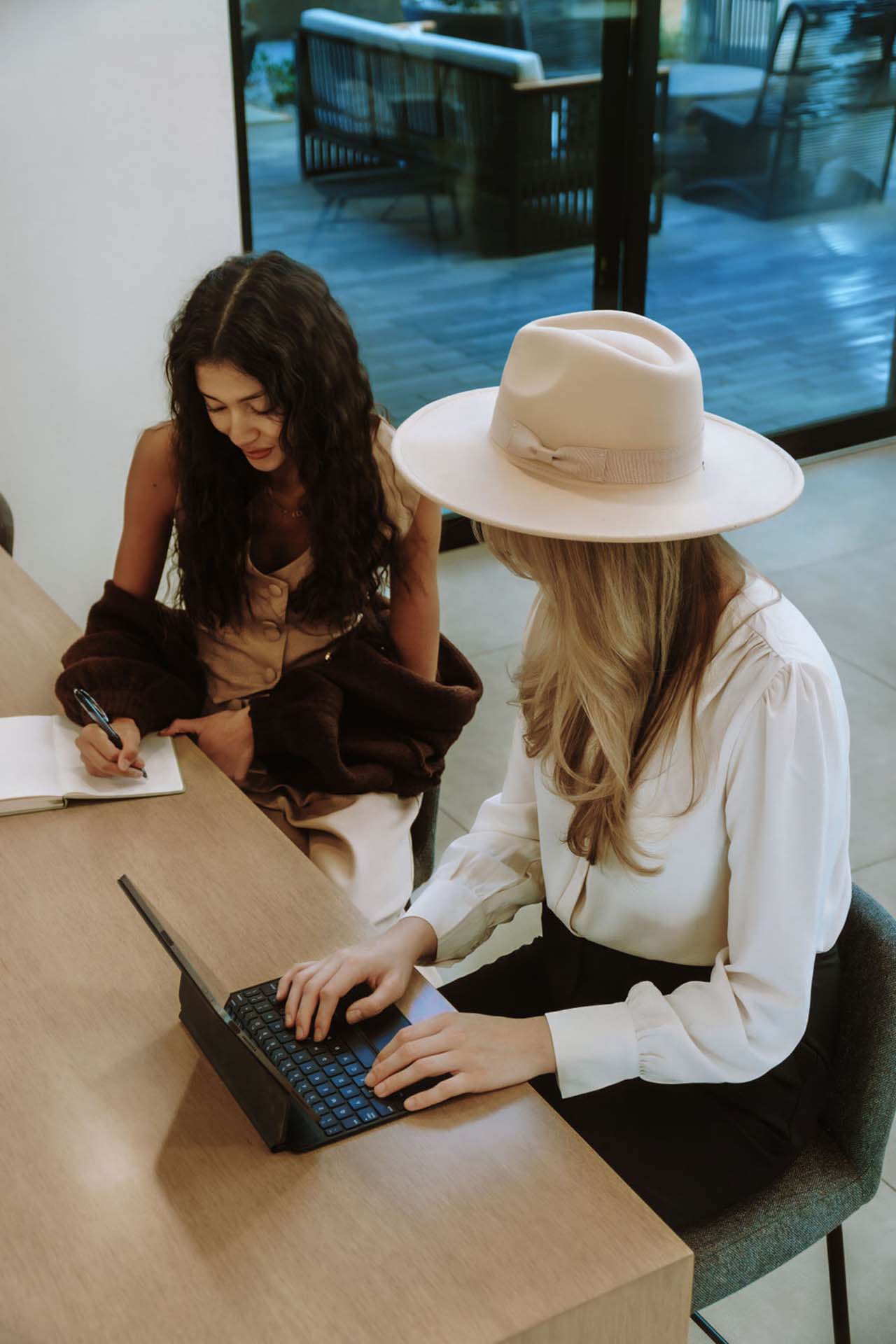 Two friends sitting together at a table with a notepad and laptop computer.