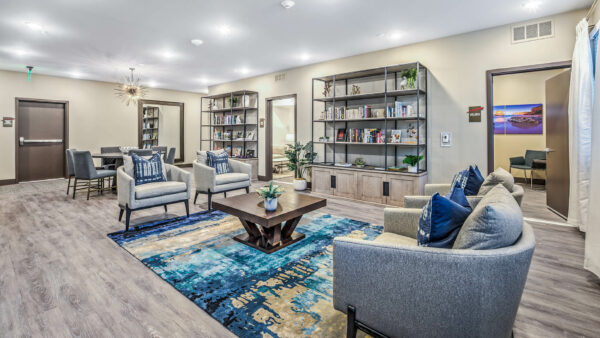 Lounge with pattern rug, plush seats, shelves with decor, and doors to wellness room.