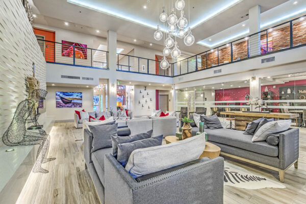 Clubroom with wood tile floor, plush couches, glass light fixture, art sculpture, and mezzanine at Inspire Apartments in Las Vegas