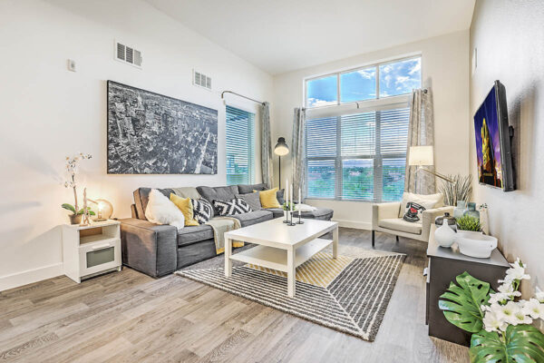 Northwest Las Vegas apartment living room with wood floor, plush sectional, tables with decor, artwork, TV, and large window.