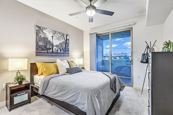 Las Vegas apartment bedroom with carpet, wood bed with headboard, bedside chests with lamps, and balcony door.