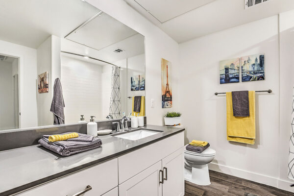 Bathroom in Las Vegas apartment with white cabinets, grey counters, large mirror, and tiled shower tub.