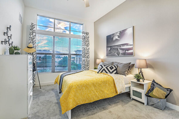 One-bedroom Las Vegas apartment with carpet, wood bed with headboard, bedside chests with lamps, and large window.
