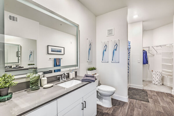 Bathroom in Northwest Las Vegas apartment with white cabinets, grey counters, large mirror, and tiled shower tub.