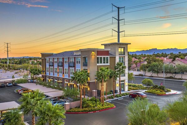 Inspire Apartments in Las Vegas with modern architecture, lush landscaping, tall palms, and ample covered parking.