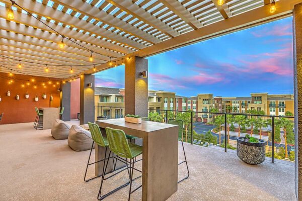 Rooftop patio at Inspire Apartments in Las Vegas with large tables, stools, plush chairs, and planters overlooking courtyard.
