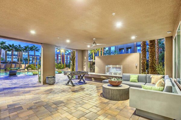 Outdoor lounge at Inspire Apartments in Las Vegas with plush sectional, foosball table, ceiling fan, and large fireplace.
